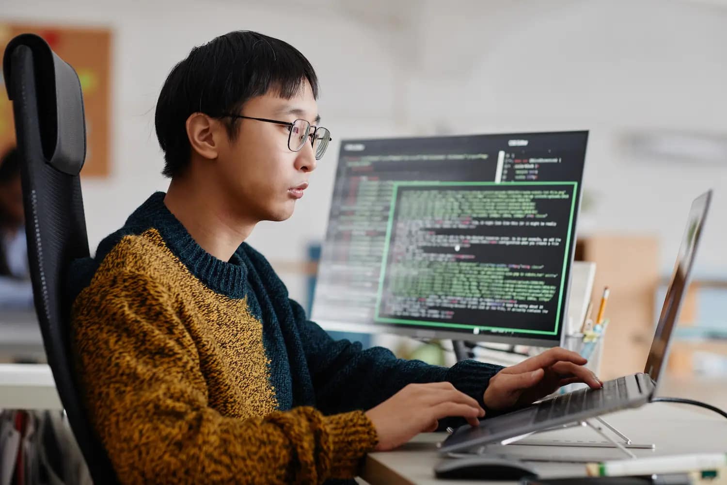 jeune homme trentenaire travaillant sur trois ordinateurs pour créer son script Python