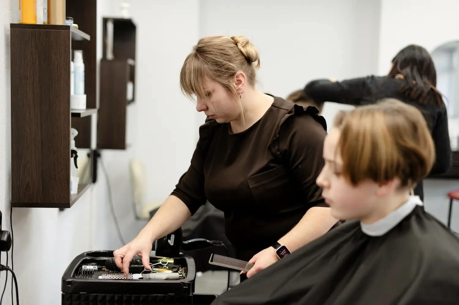 femme en train de chercher ses outils de coiffure pour coiffer une cliente apres s'être reconvertie au métier de coiffeuse