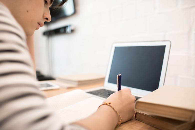 jeune homme étudiant prenant des notes sur les formations et études en alternance qu'il veut faire sur Parcoursup devant son ordinateur portable